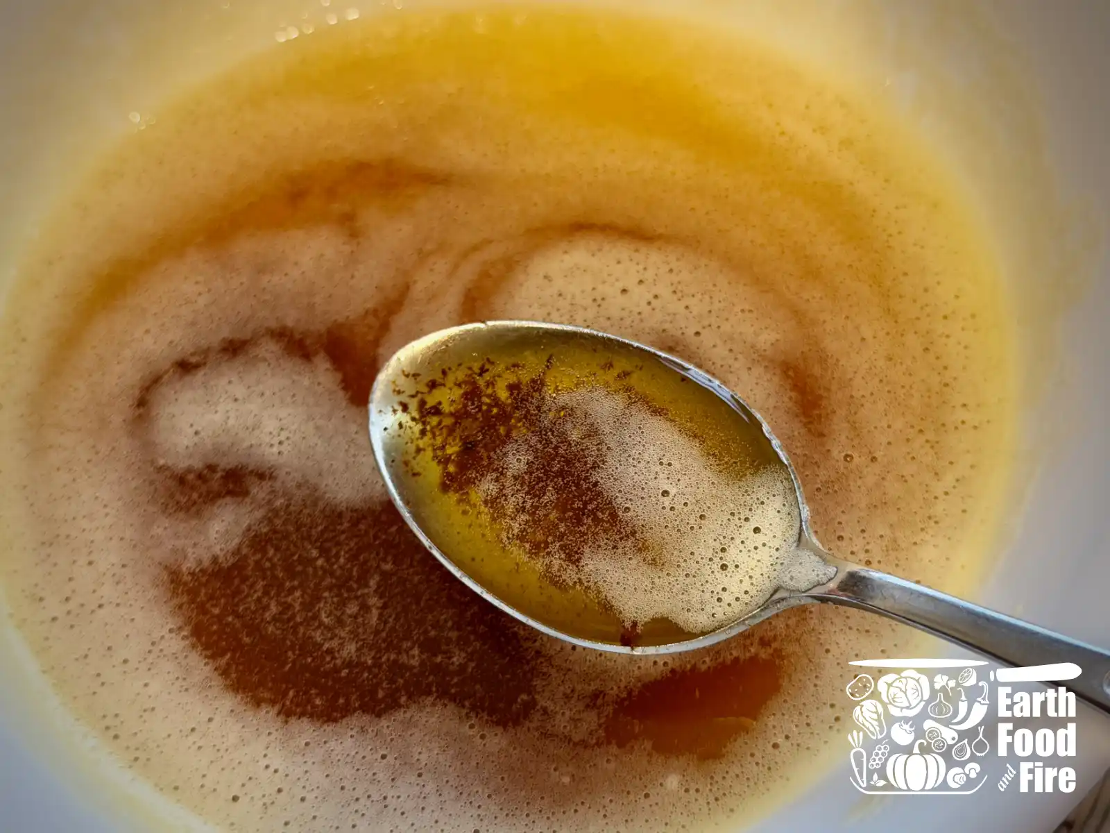 A spoonful of browned butter held over the bowl, showing the browned milk specs