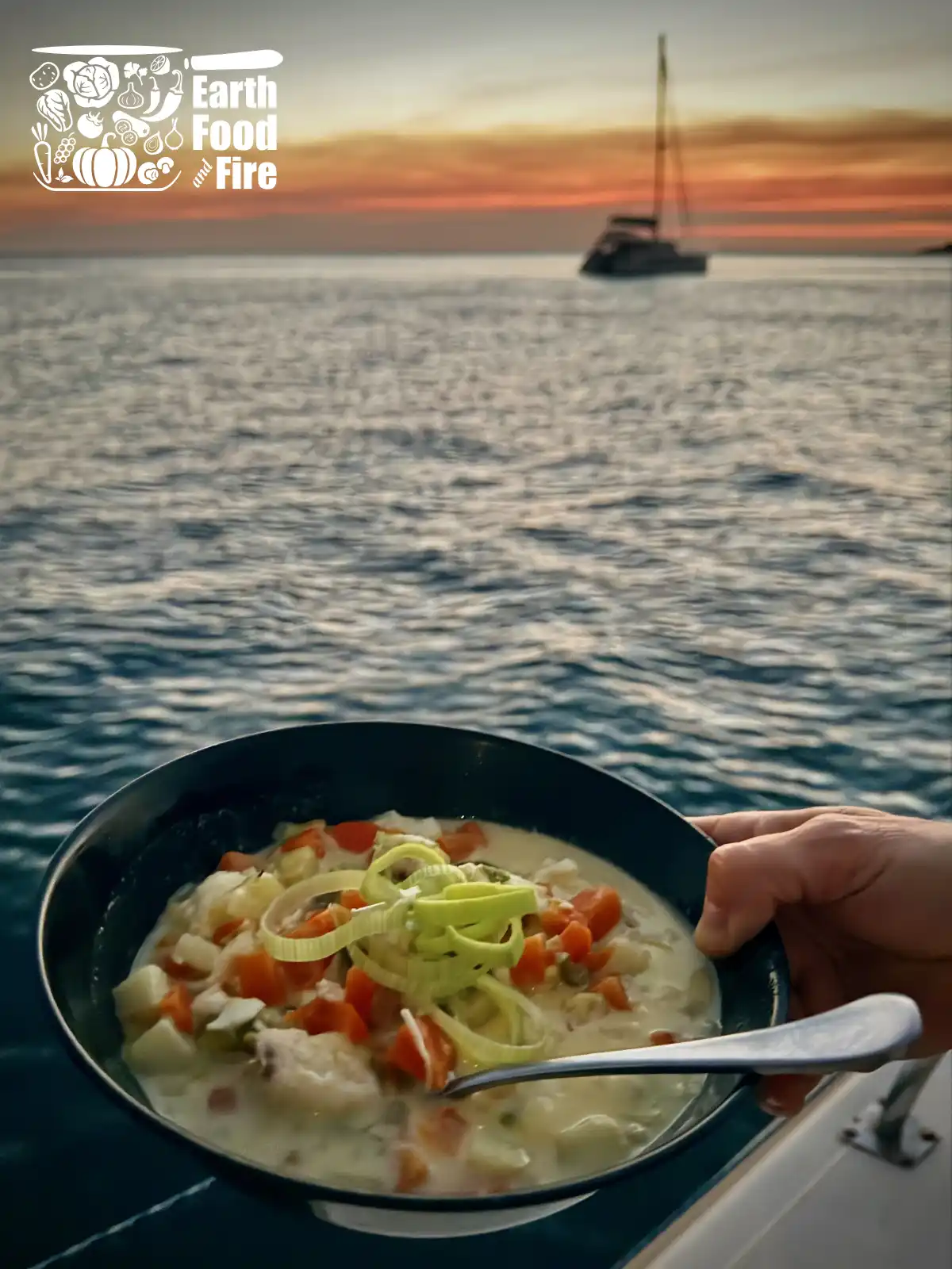 A steaming bowl of cod fish chowder with chunks of white fish, potato, carrot, and leek in a creamy broth, garnished with fresh leek.
