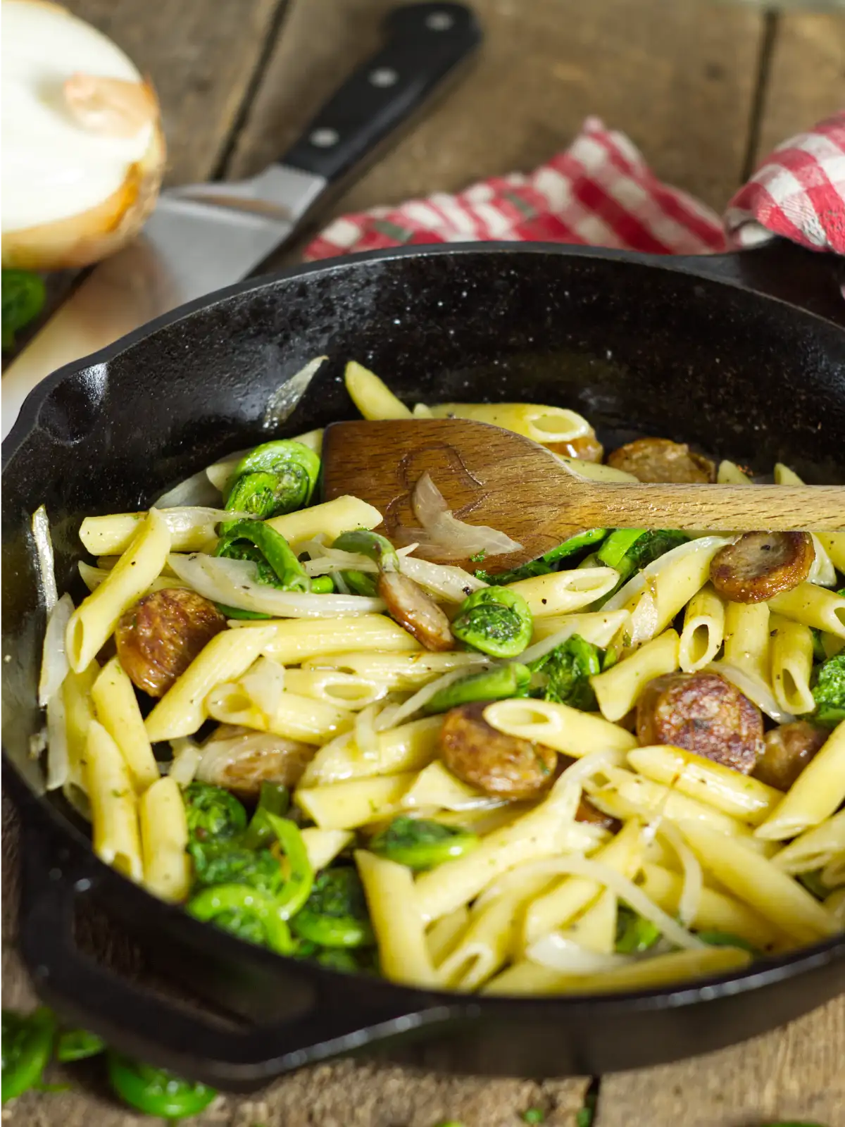 Fiddlehead sausage penne in a skillet on a wooden table