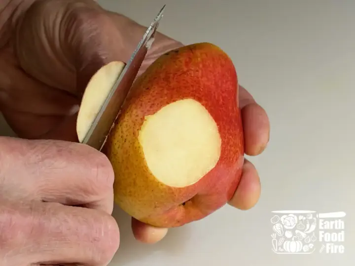 Detailm of hand slicing off the rounded bottom of pear half with a small pairing knife.