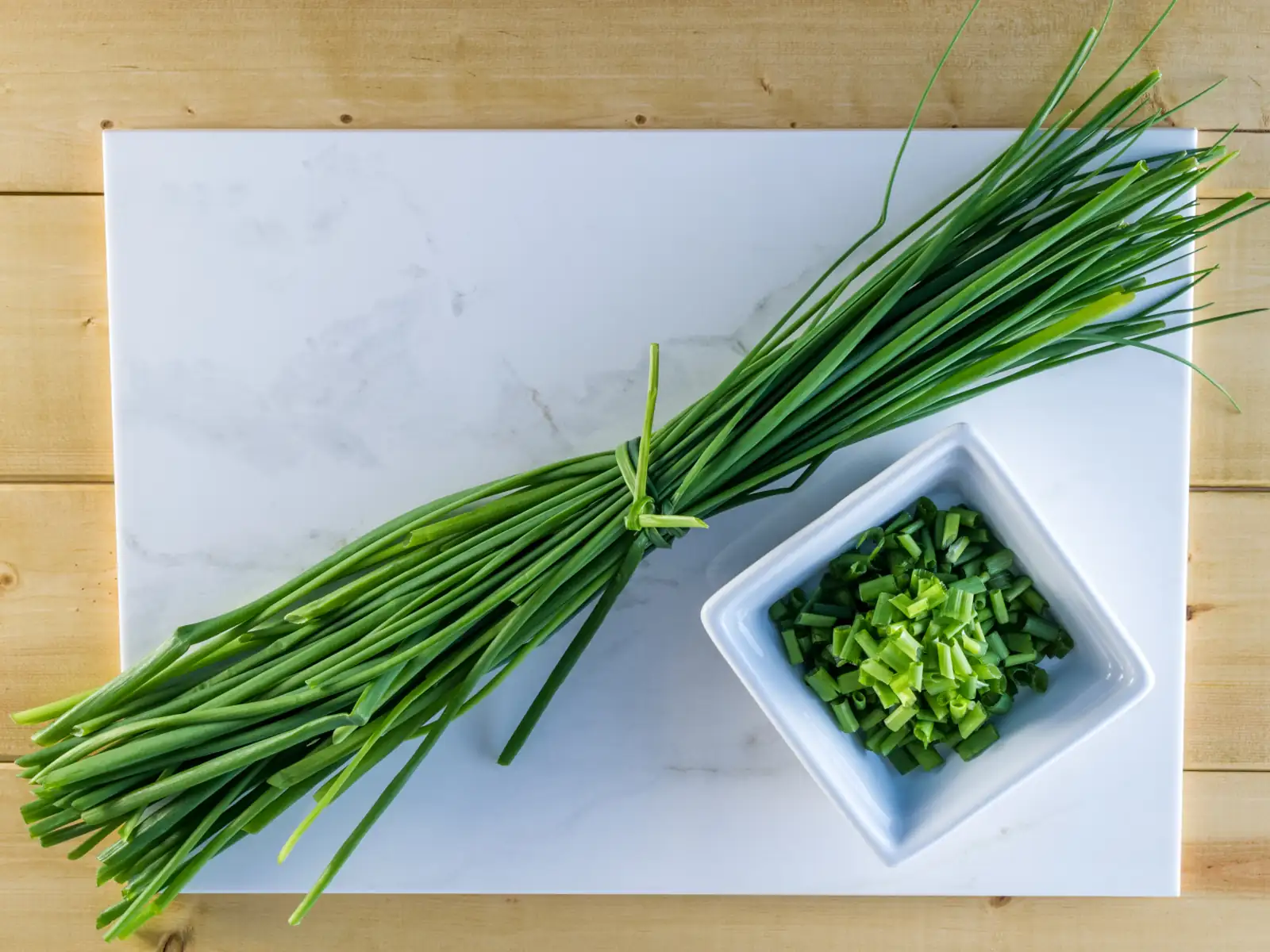Freshly harvested chives - bunch on the cutting board and a chopped chives in a bowl