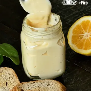 Creamy homemade mayonnaise recipe in a jar on a wooden table with a toasted bread and half of a lemon