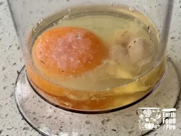Egg, mustard, and vinegar at the bottom of a tall jar with golden olive oil floating on top
