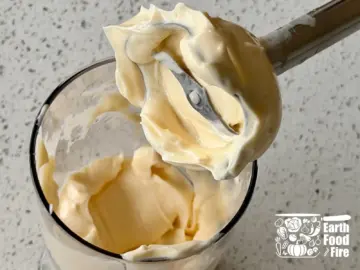 Stick mixer lifting a thick peak of finished homemade mayonnaise out of a jar.