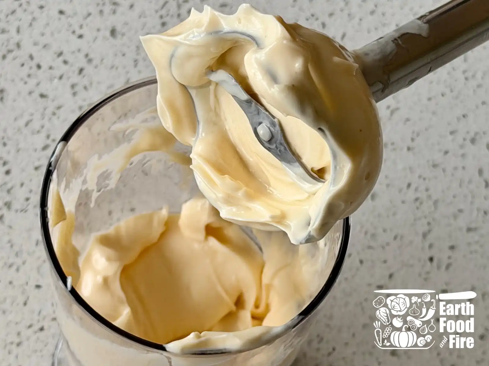 Stick blender lifting a thick peak of finished homemade mayonnaise out of a jar.