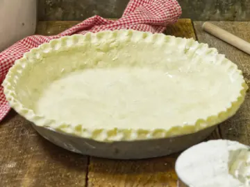 Homemade pie shell on a wooden table, with a kitchen towel
