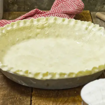 Homemade pie shell on a wooden table, with a kitchen towel