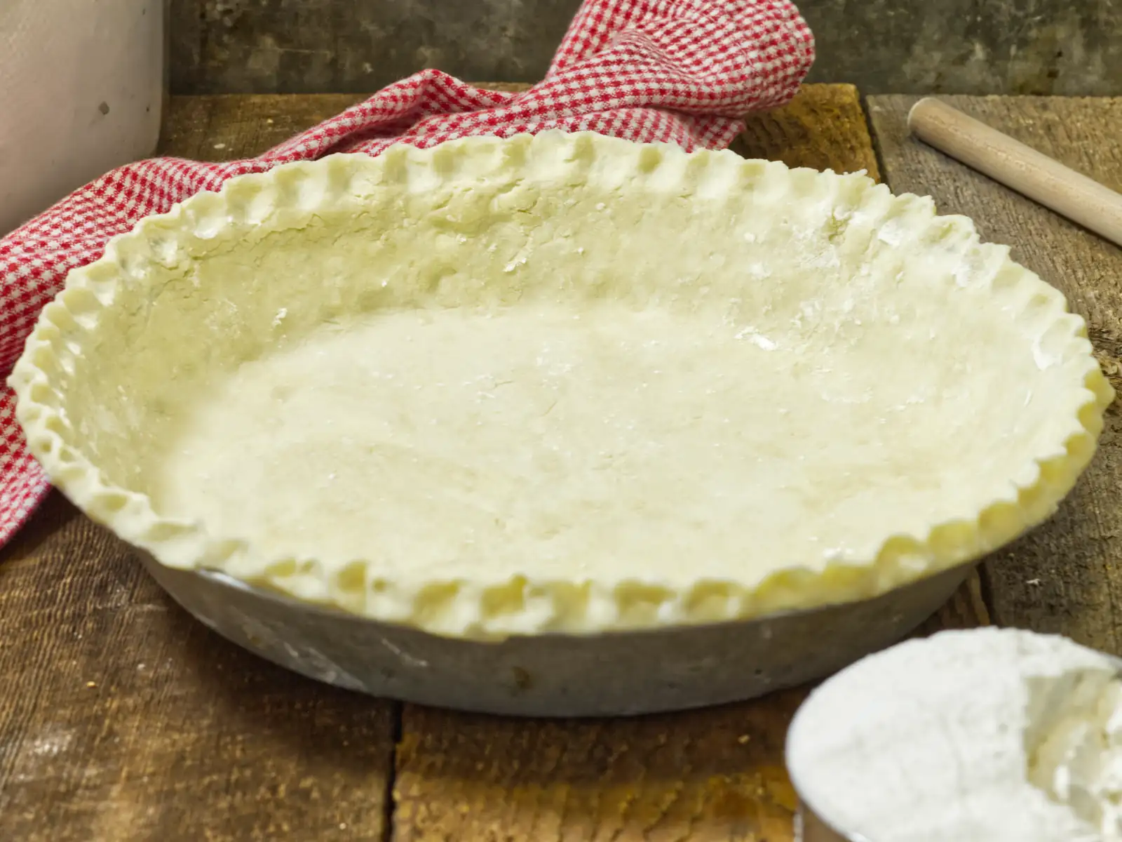 Homemade pie shell on a wooden table, with a kitchen towel