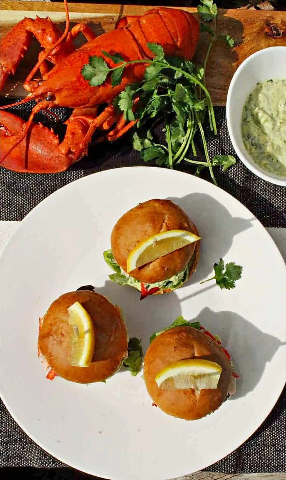 Lobster sliders on a plate, with lobster, cilantro and mayonnaise in the background