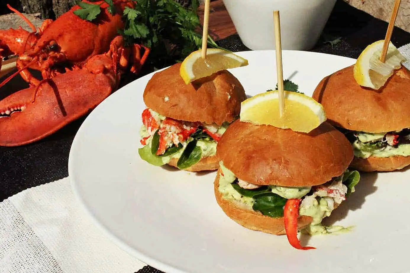 Lobster sliders served on a plate, with lobster in the background