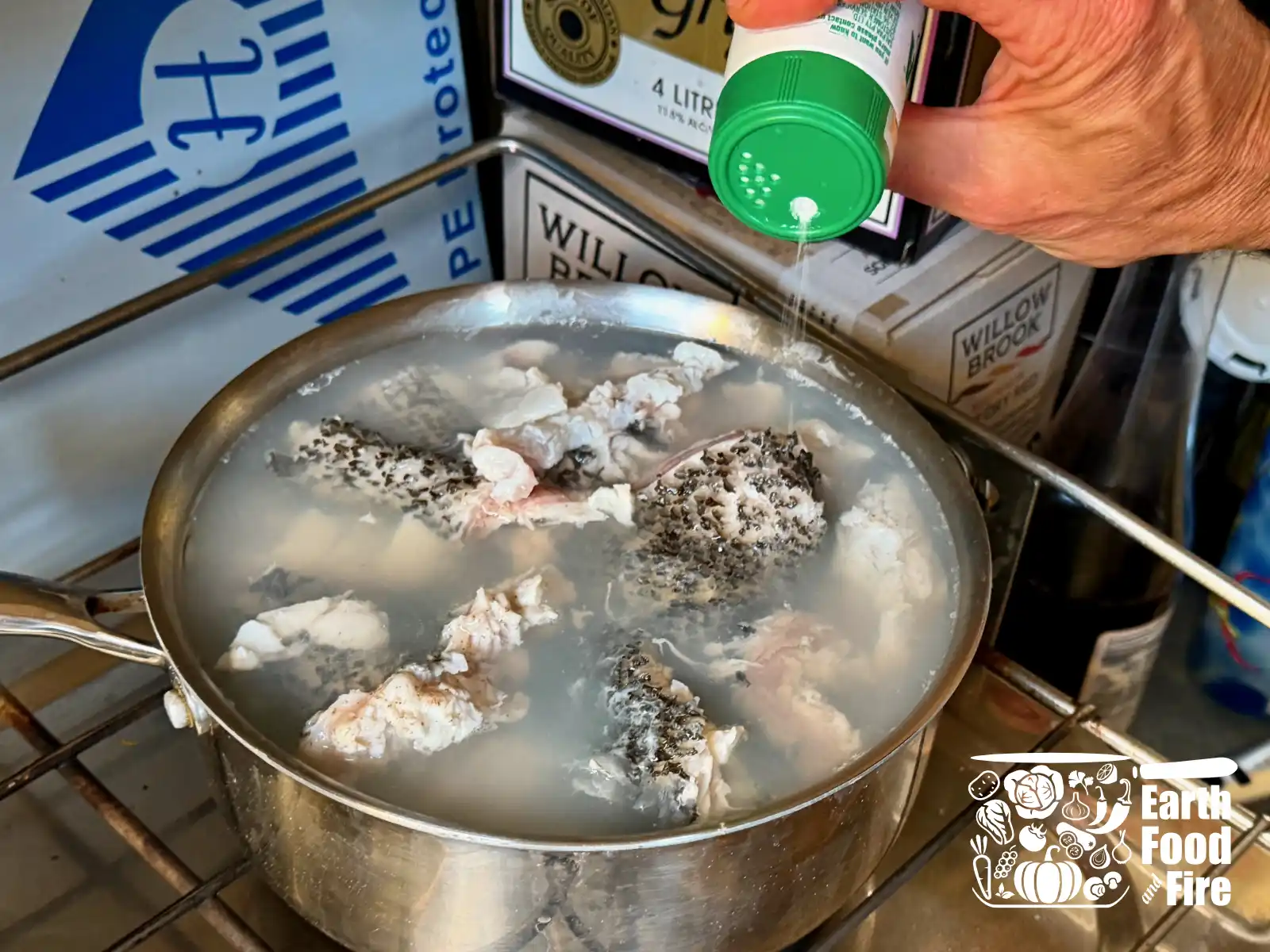 A pot with homemade fish stock - water and fish offcuts - boiling on the stove, and a hand adding some salt.