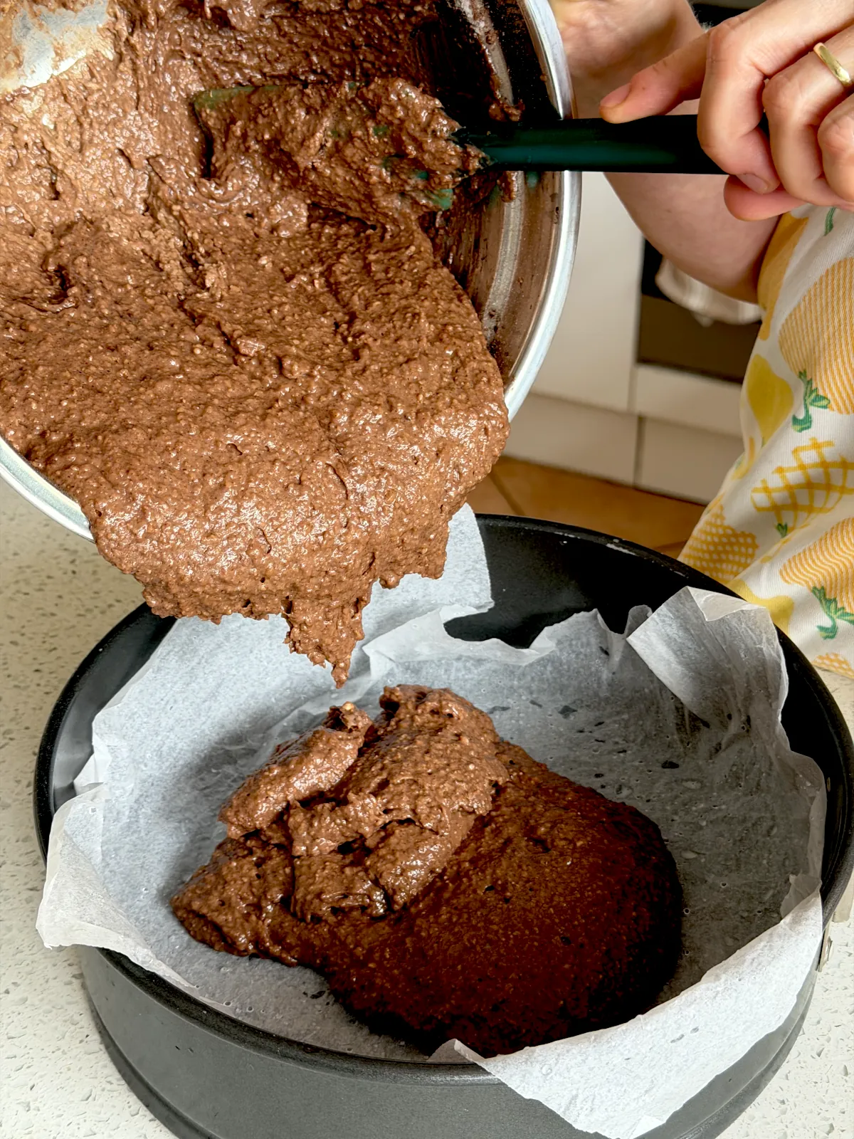 Pouring the chocolate cake mix into the round baking pan lined with parchment paper