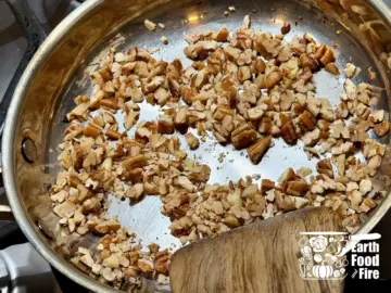 Roughly chopped pecan nuts being rosted in a stainless steel pan