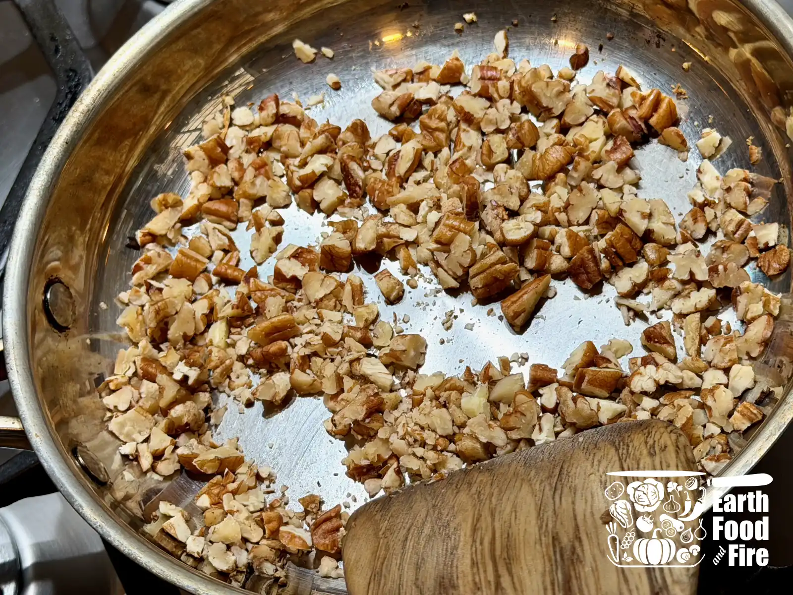 Roughly chopped pecan nuts being rosted in a stainless steel pan