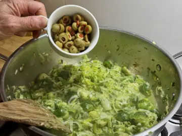 Adding stuffed olives to sauteed Brussels sprouts mix.