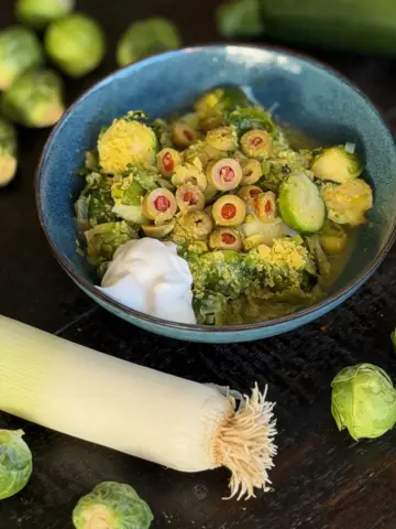 Sautéed Brussels sprouts with caramelized edges, sweet leeks, and green olives in a serving bowl, topped with a dollop of Greek yogurt.