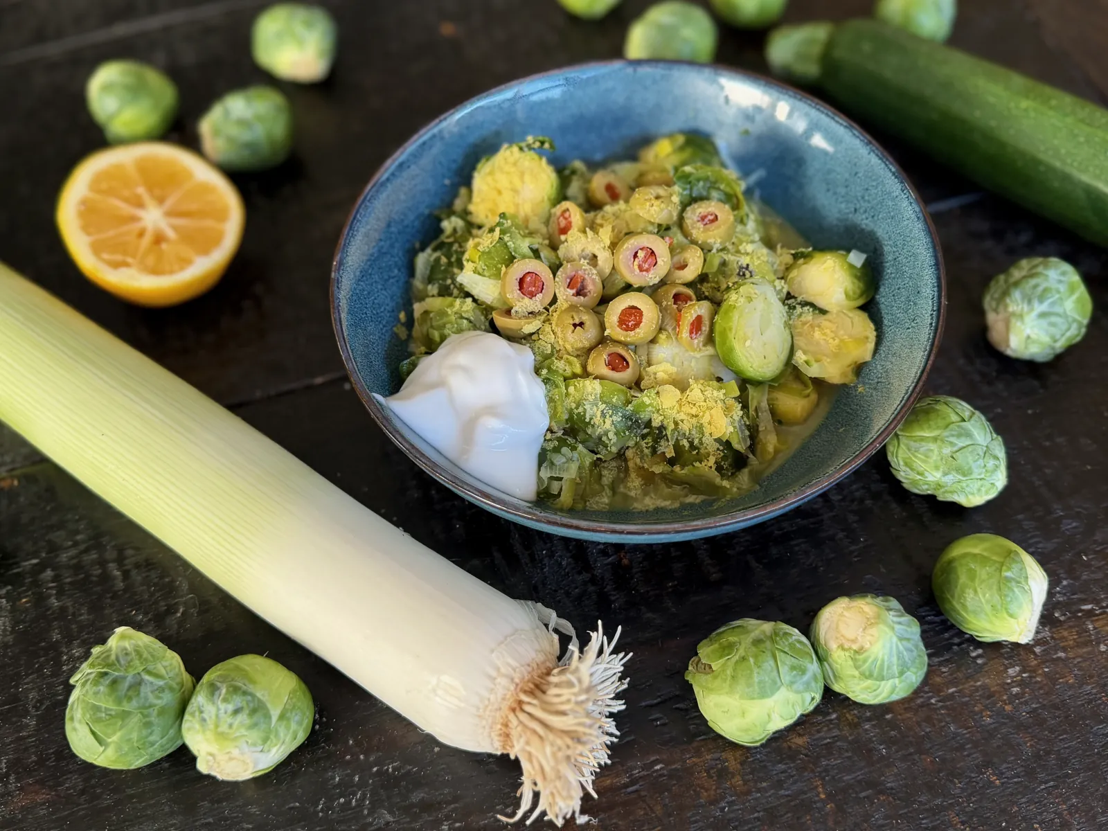 Sautéed Brussels sprouts with caramelized edges, sweet leeks, and green olives in a serving bowl, topped with a dollop of Greek yogurt.