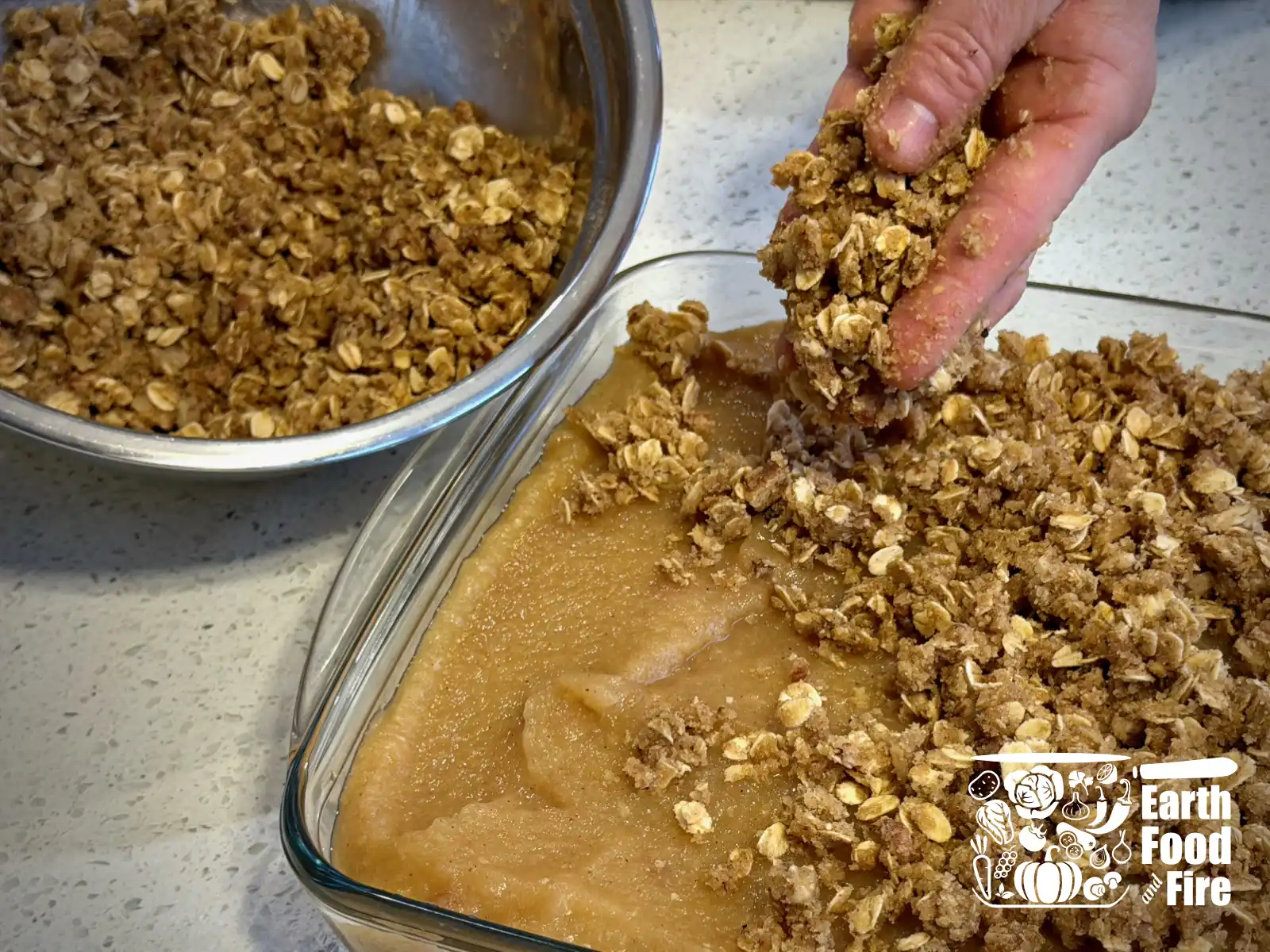 The crumble topping being scattered by hand over the applesauce filling