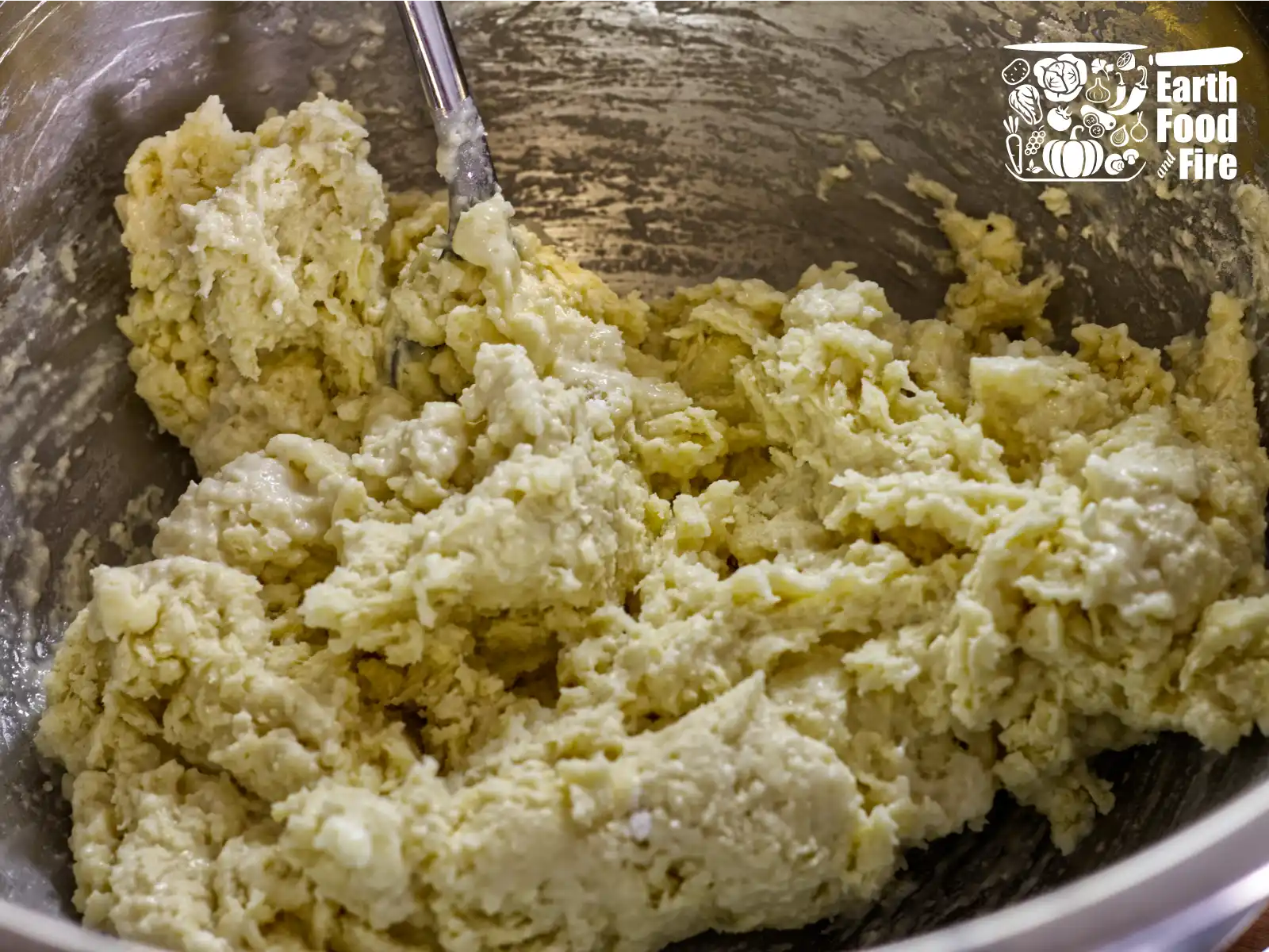 Stainless steel bowl with shaggy dough for blueberry cobbler biscuit topping being mixed bith sppoon