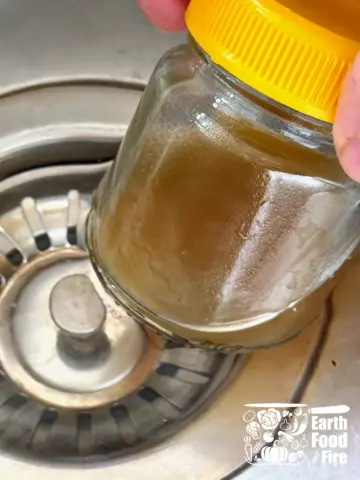 Jar of honey lemon dressing being warmed in a hot water bath in sink