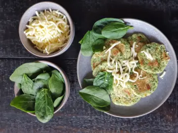 Spinach and cheese mini pancakes with fresh spinach leaves and grated cheese