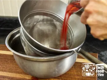 Straining raspberry cordial through a fine mesh