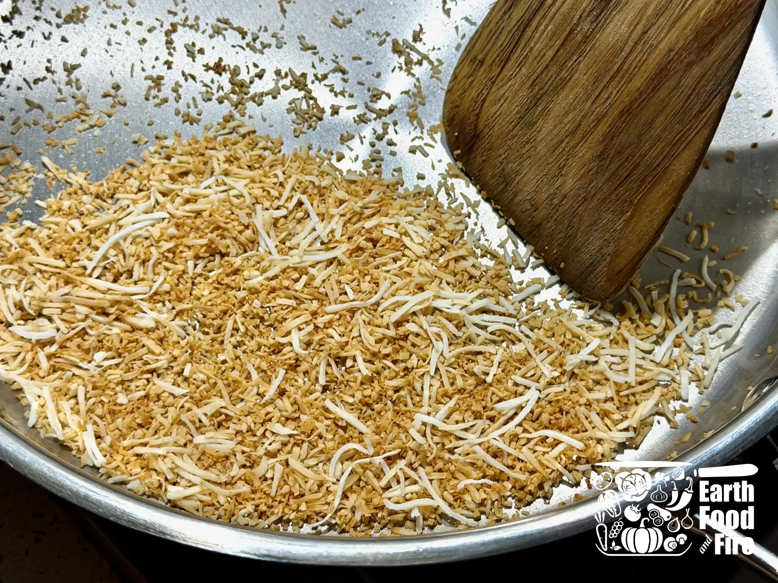 Shredded coconut turning golden brown in a pan with wooden spoon stirring